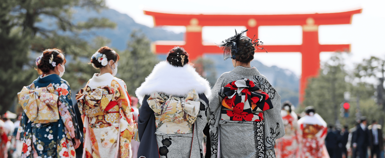 Geisha walk towards a large torii gate in a cultural event in Japan